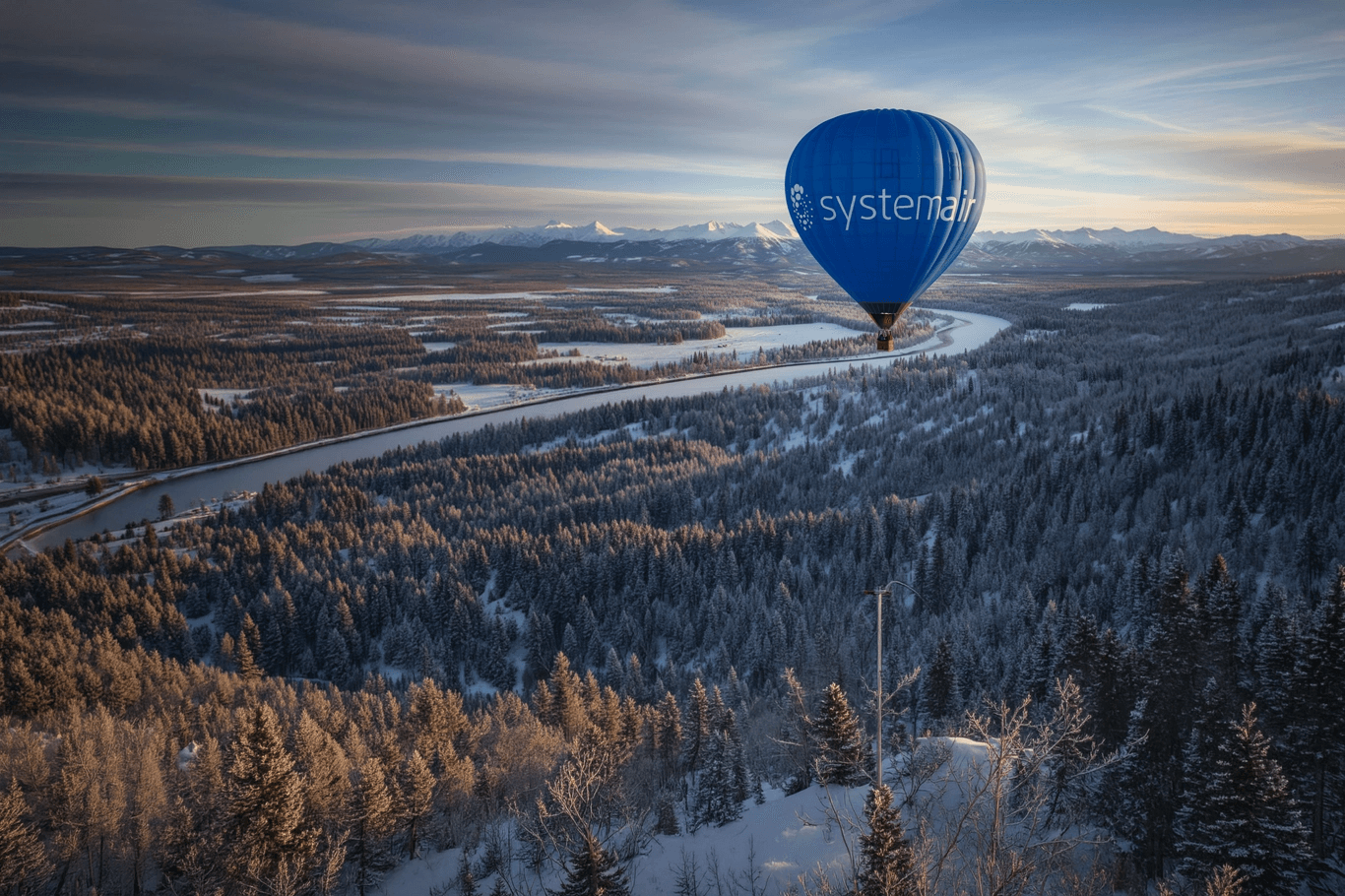 A blue hot air balloon floats above a lush green landscape with distant mountains under a clear sky.