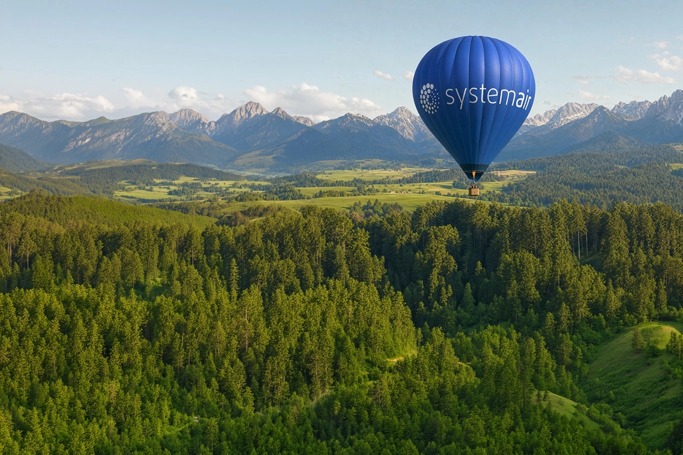 A blue hot air balloon floats above a lush green landscape with distant mountains under a clear sky.